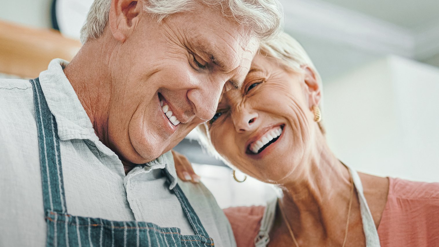 Älteres Ehepaar steht lächelnd in der Küche beim Kochen