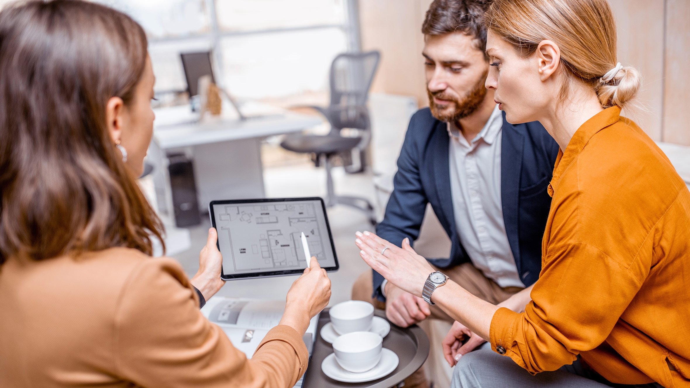 Drei Personen diskutieren im Meetingraum über ein Tablet. Eine Frau zeigt auf das Display, während die anderen aufmerksam zuhören.