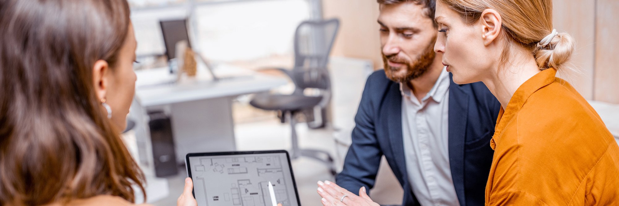 Ehepaar schaut mit der Immobilienberaterin ins Tablet